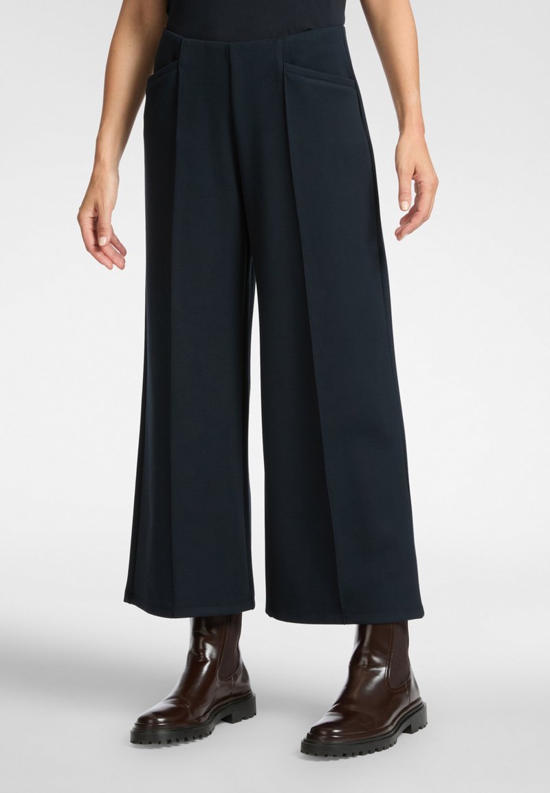 Kalhoty s širokými nohavicemi z tmavě námořnické látky s předními kapsami, s přesně tvarovaným střihem a hladkou texturou, doplněné hnědými kotníkovými botami.