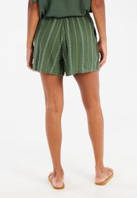Shorts verts avec des rayures verticales jaunes et blanches, dotés d'une taille élastique et d'une coupe loose, fabriqués en tissu léger et texturé.