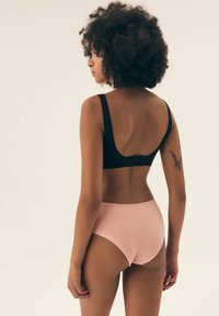 Czarny bezszwowy stanik z szerokimi ramiączkami i zapięciem na haftki, w komplecie z jasnoróżowymi majtkami o wysokim stanie, prezentującymi gładką bawełnianą strukturę.