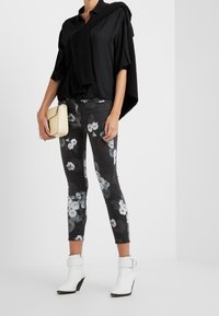 Zwarte oversized shirt met een gebreide trui eroverheen. Zwart jeans met bloemmotief en witte enkellaarsjes. Beige tas.