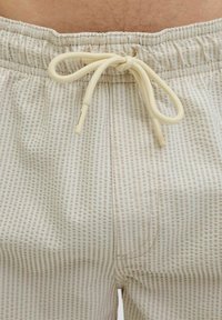 Lysfarvede shorts med et tekstureret stribet mønster. Har en elastisk talje med snøre og sidelommer.