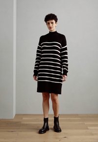 Robe à rayures noires et blanches avec un col montant, des manches longues et une coupe décontractée, associée à des bottines noires.