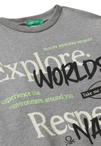 Felpa grigia con testo a caratteri misti che include "Esplora," "Mondi," "Rispetto," "Associazione Faunistica Presenta," e "sperimenta l'ambiente che ti circonda."