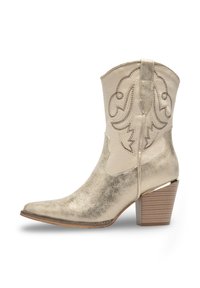 Bottine métallique dorée avec un bout pointu, des coutures décoratives et un talon empilé. Texture lisse avec une finition légèrement patinée.