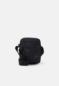 Borsa a tracolla nera con cintura regolabile, decorata con numerosi piccoli loghi di coccodrillo ricamati in verde sul davanti e sui lati.