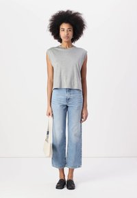 Gray cropped sleeveless top, light blue wide-leg jeans, black slip-on shoes, holding a beige tote bag. Simple design with a relaxed fit.