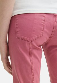 Różowe dżinsy o gładkiej fakturze, z dwoma tylnymi kieszeniami i widocznymi szwami wzdłuż szwów. Zbliżenie na tylny widok.