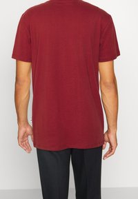 Bordeauxrotes Kurzarm-T-Shirt mit lockerer Passform, glatter Baumwolltextur und einem abgerundetem Ausschnitt. Verfügt über minimale Nähte und ein Etikett am Saum.
