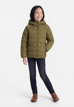 Child smiling, wearing an olive green padded jacket with hood, black jeans, and brown ankle boots, standing against a white background.