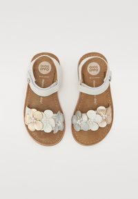 Sandalias de cuero de color claro con una correa de velcro, adornadas con embellishments de flores metálicas y texturizadas en plata y beige.