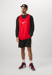 Rød Nike trenings tanktop over en svart langermet skjorte, svarte shorts og røde Nike høye sneakers med hvite detaljer. Urban stil.