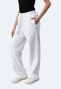 Weiße Baumwoll-Sweatpants mit einer lockeren Passform, elastischem Bund, Kordelzug und Seitentaschen, kombiniert mit weißen Sneakers.