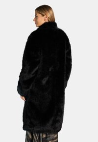 Cappotto in pelliccia sintetica nera con colletto alto, texture morbida, vestibilità over e maniche lunghe, caratterizzato da una finitura liscia e una silhouette elegante.