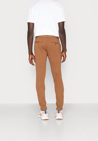 Bruna slim-fit byxor med två bakfickor, knäppning med knappar och en slät yta. Bärs med en vit t-shirt och ljusa sneakers.