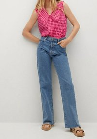 Blouse sans manches à carreaux roses avec un col Claudine, associée à un jean bleu clair taille haute à jambes droites et des sandales couleur sable.