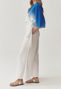 Pantalones de pierna ancha blancos combinados con una blusa en degradado de azul a blanco, que presenta mangas cortas y un cinturón atado en la cintura, complementados con sandalias planas.