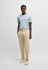 Light blue short-sleeve t-shirt, beige chinos, and cream sneakers. Casual fit with a round neck and subtle branding on the tee.