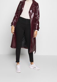 Viininpunainen, kiiltävä trenssitakki, jossa isot kaulukset, sivutaskut ja säädettävät hihansuut, yhdistetty mustiin kapeisiin housuihin ja valkoisiin lenkkareihin.