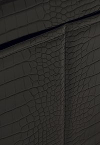 Sac en similicuir noir avec un motif texturé effet peau de crocodile, présentant des coutures surpiquées et une finition lisse.