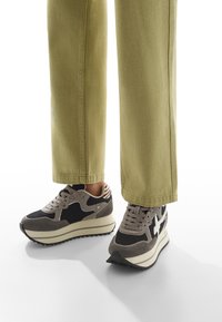Gray and black sneakers with a textured upper, mesh panels, and a layered sole. Complemented by khaki wide-leg pants.
