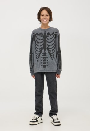 Maglietta grigia a maniche lunghe con stampa di scheletro nera, abbinata a jeans scuri e scarpe sportive bianco e nere. Tessuto morbido, vestibilità comoda.