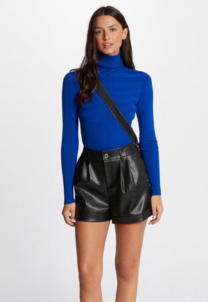 Top de cuello alto acanalado azul combinado con pantalones cortos de cuero sintético negro de tiro alto; presenta un diseño ajustado y una sutil textura horizontal.