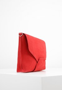 Punainen mokkanahkainen clutch-laukku, jossa on kolmioaitta, ommellut reunat ja pieni etutasku. Liu'utettu pinta, joka on tyylikäs muotoilu.