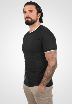 Camiseta negra de manga corta con un patrón texturizado, detalles en blanco en el cuello y las mangas, combinada con pantalones en tono arena claro.