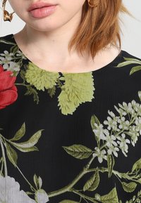Vestido negro floral con grandes hojas y flores rojas y verdes. Textura suave con escote redondo y mangas cortas.