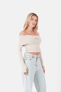 Beige, schulterfreies, geripptes Crop-Top mit langen Ärmeln, das ein kleines Logo auf der Vorderseite hat, kombiniert mit hellblauen, hochtaillierten Jeans.