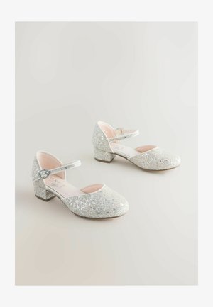 Pantofi argintii sclipitori cu vârf rotund, curea la gleznă și toc bloc jos. Partea superioară are o textură strălucitoare și un interior roz neted.