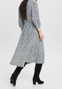 Abito lungo a pattern bianco e nero con vita arricciata e maniche a palloncino, abbinato a stivali neri al ginocchio.
