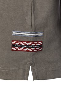 Olive green fabric with a textured finish; features a patch pocket with red, white, and black geometric patterns and branding detail.