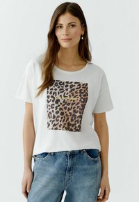 T-shirt blanc à manches courtes avec un motif léopard en forme de carré et des lettres dorées. Coupe décontractée avec un col rond et une texture douce.