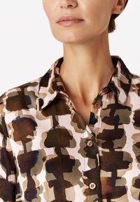 Collared shirt in a multicolored abstract print featuring earthy tones of brown, beige, and green. Soft fabric with button detailing.