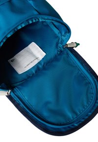 Zilas mugursomas iekšpuse ar gludu, rievotu tekstūru. Ir nodalījums ar rāvējslēdzēju un etiķete ar uzrakstu "ŠĪ MUGURSOMA PIEDER".