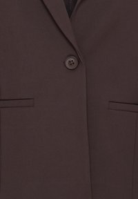 Blazer marron foncé avec un seul bouton noir fermé et deux poches horizontales fendues à l'avant.