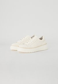 Witte sneakers met textiel, ronde neus en contrasterende gevlochten details langs de zool. Vetersluiting en zachte voering zichtbaar.