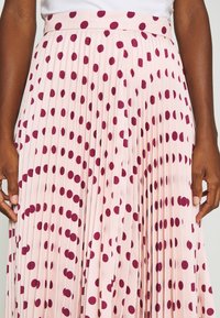 Pleated skirt in light pink fabric with dark pink polka dots. Features a wide waistband and flowing design, emphasizing the pleat texture.