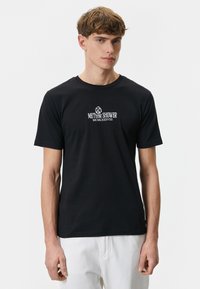 Sort bomulds T-shirt med rund hals, med hvid grafisk tekst "METEOR SHOWER MCMLXXXVIII" på brystet. Korte ærmer, klassisk pasform.