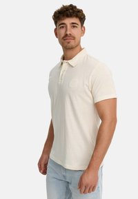 Cremfarbener Poloshirt mit kurzen Ärmeln aus weicher Baumwolle, ausgestattet mit einer knöpfbaren Leiste und einem tonal abgestimmten Logoakzent auf der Brust.
