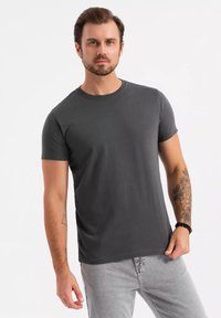 T-paita tummanharmaata lyhythihaista puuvillaa, jossa on pyöreä kaula-aukko. Sen pinta on sileä ja malli on rento. Yhdistetty kevyisiin harmaisiin farkkuihin.