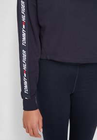 Námořnické triko se zkráceným střihem, elastickými manžetami, s bílým logem "TOMMY HILFIGER" běžícím vertikálně podél levého rukávu.
