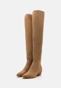 Bottes en daim beige montant jusqu'au genou, avec un bout pointu et un petit talon empilé. Texture lisse et design ajusté. Aucune pièce métallique visible ni motif.