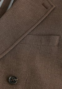 Blazer en tissu marron texturé avec revers cranté, poche passepoilée et bouton rond foncé en détail.