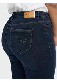 Mörkblå denimjeans med hög midja, med en brun läderetikett bak och en distinkt fickdesign med sömdetaljer.