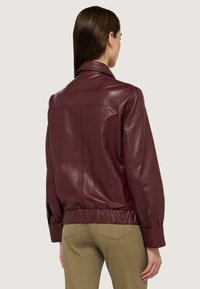 Giacca di pelle bordeaux con una texture liscia, design corto e vita elastica. Presenta un colletto classico e maniche lunghe.