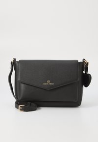 Sac bandoulière en cuir noir avec une finition texturée, matériel doré, fermeture à rabat et bandoulière détachable. Présente un logo gaufré à l'avant.