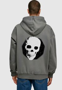 Felpa grigia con cappuccio, caratterizzata da una grande grafica di teschio bianco e nero sul retro, con vestibilità rilassata e polsini a coste.