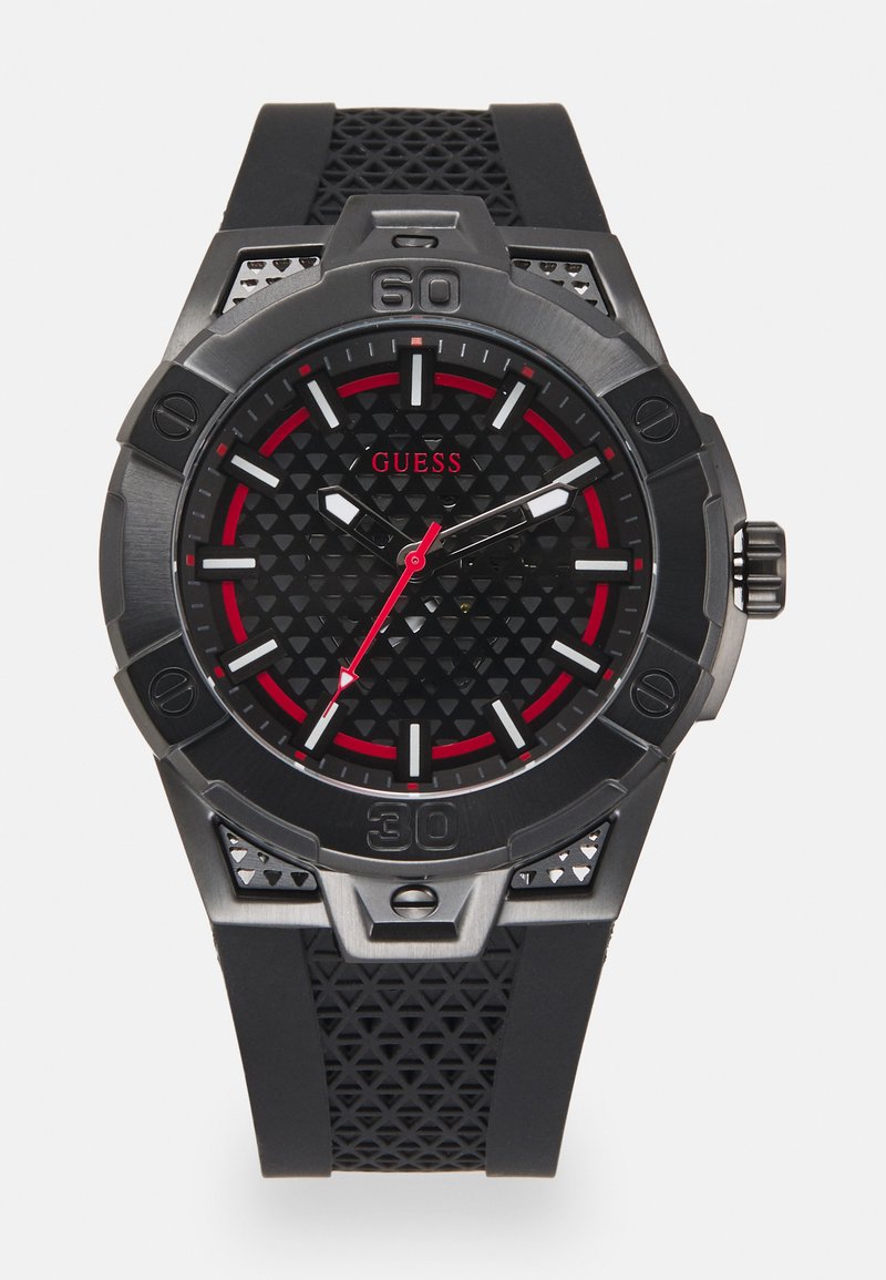 Reloj con correa de goma negra, esfera negra texturizada, acentos rojos y herrajes plateados. Presenta una caja audaz y marcadores de hora elevados.